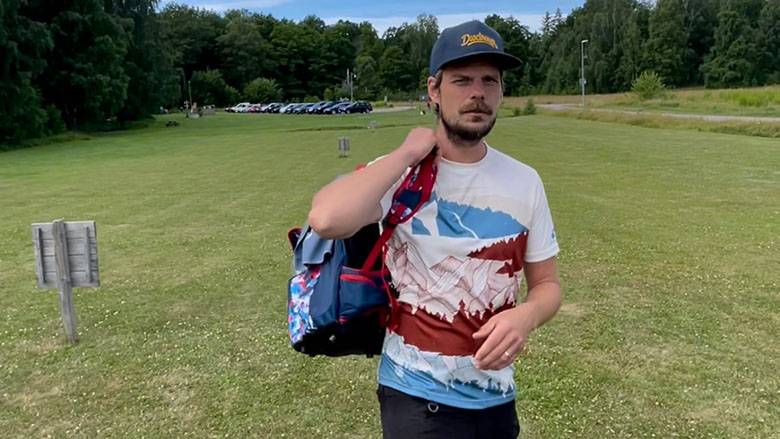 Discgolfens trickshot-guru Erik Karlgren med väskan i hand ute på discgolfbanan.